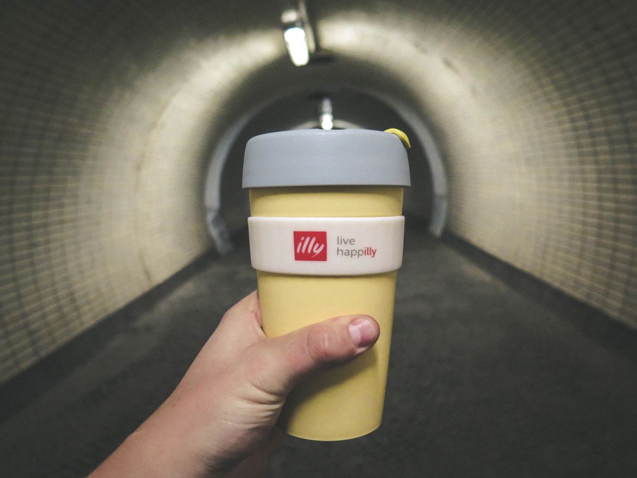 gallery-2 Perspective shot of a hand holding a reusable coffee cup inside a dimly lit tunnel.